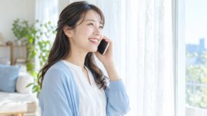 窓辺でスマホを耳に当てて笑顔で話す女性