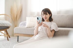自宅のソファの前でスマホを見ながら微笑む女性